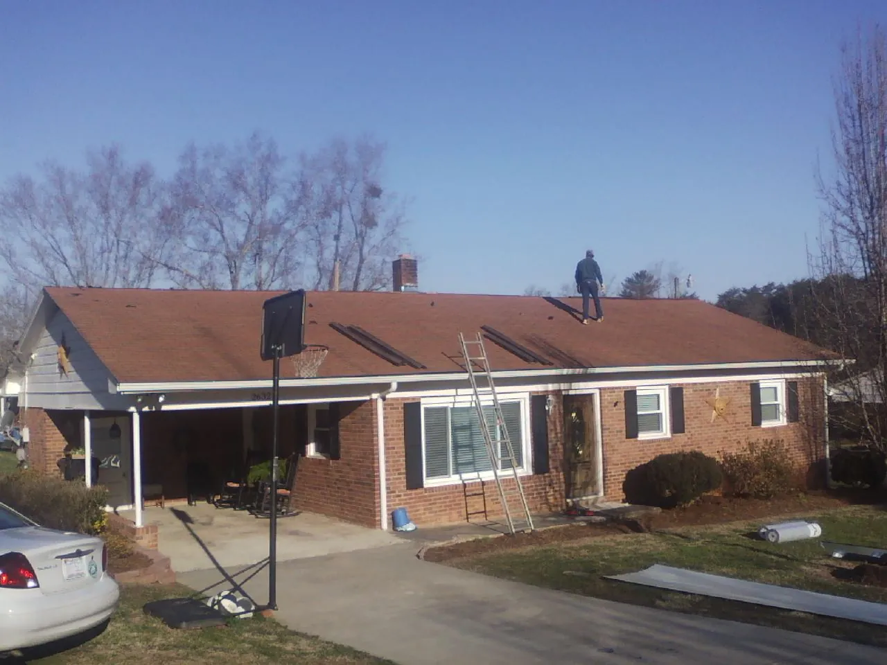 Roofer stripping a shingle roof on a brick ranch before metal panels in Newfield
