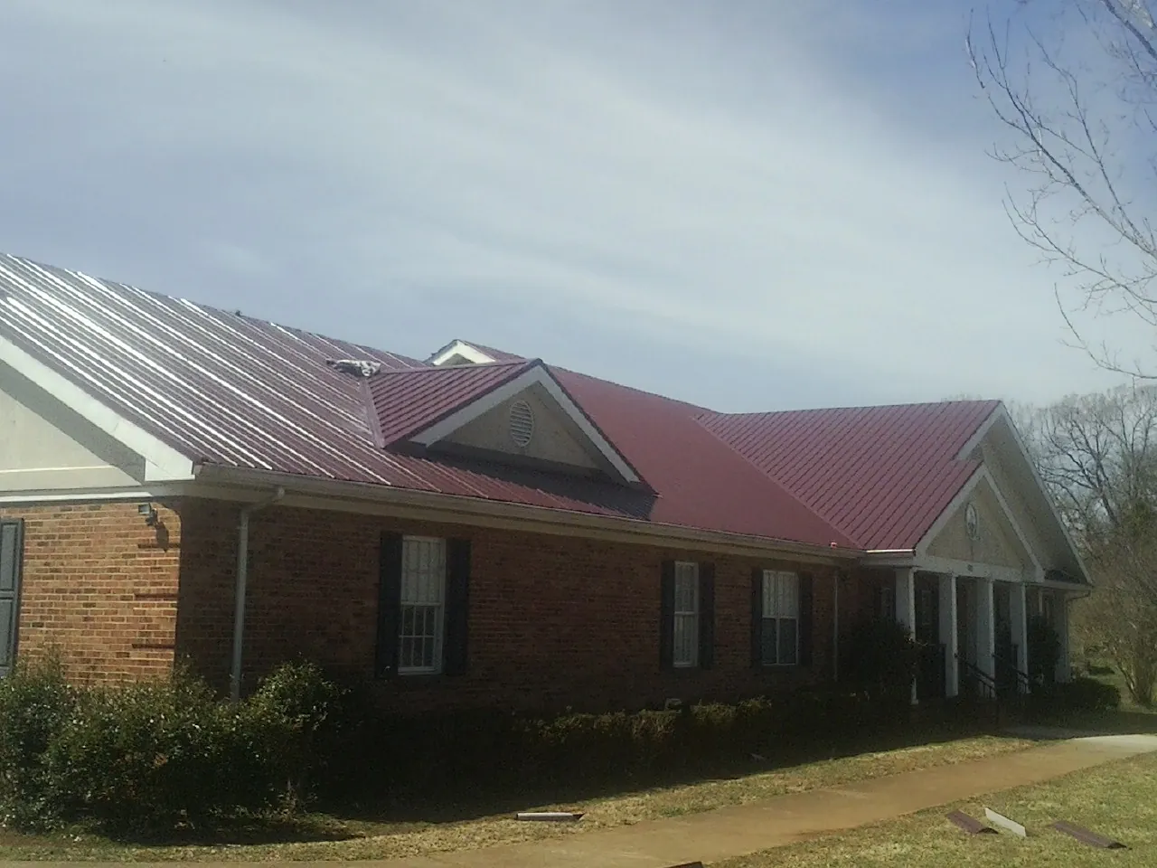 Red metal roof with gabled entries on a long brick building, from a Hail Damage Roof Repair job in Newfield