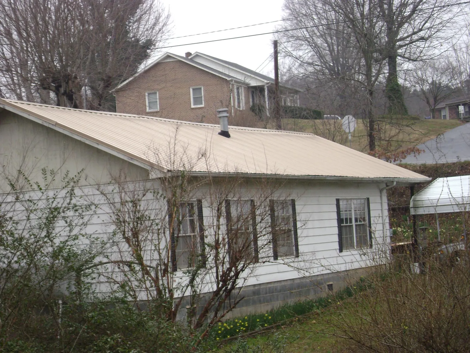 Tan metal roof on a white sided house set into a hillside — Commercial Roofing by Roofing Brothers in Newfield