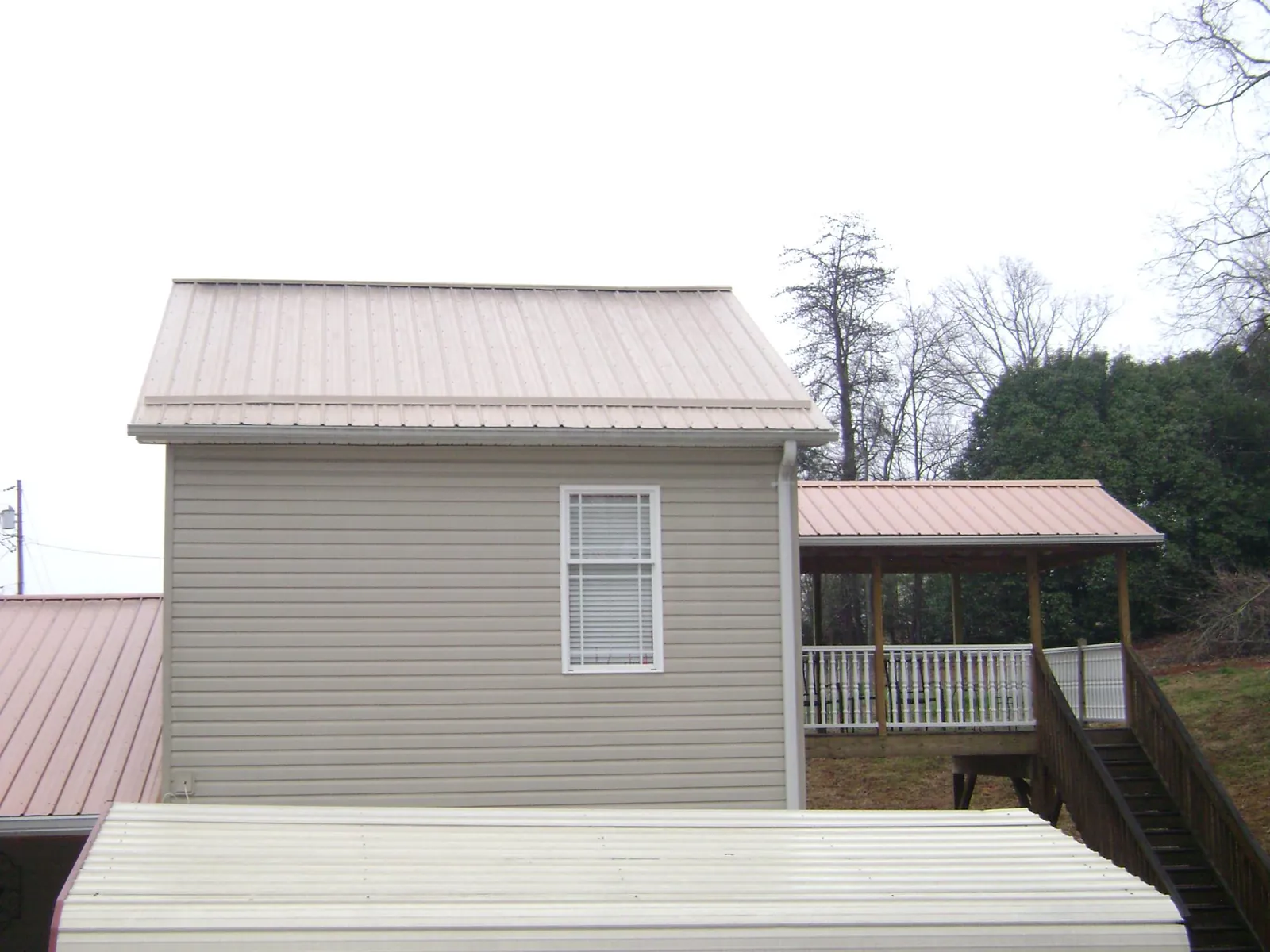 Tan metal roofs on a two story addition and attached porch, from a Roof Replacement job in Newfield